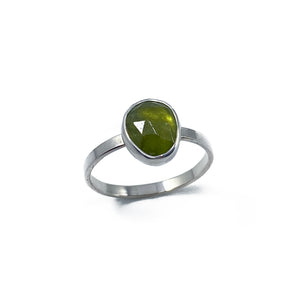 A minimal ring made of silver, boasting a faceted vesuvianite stone. In this photo it is standing upright on an all white background.